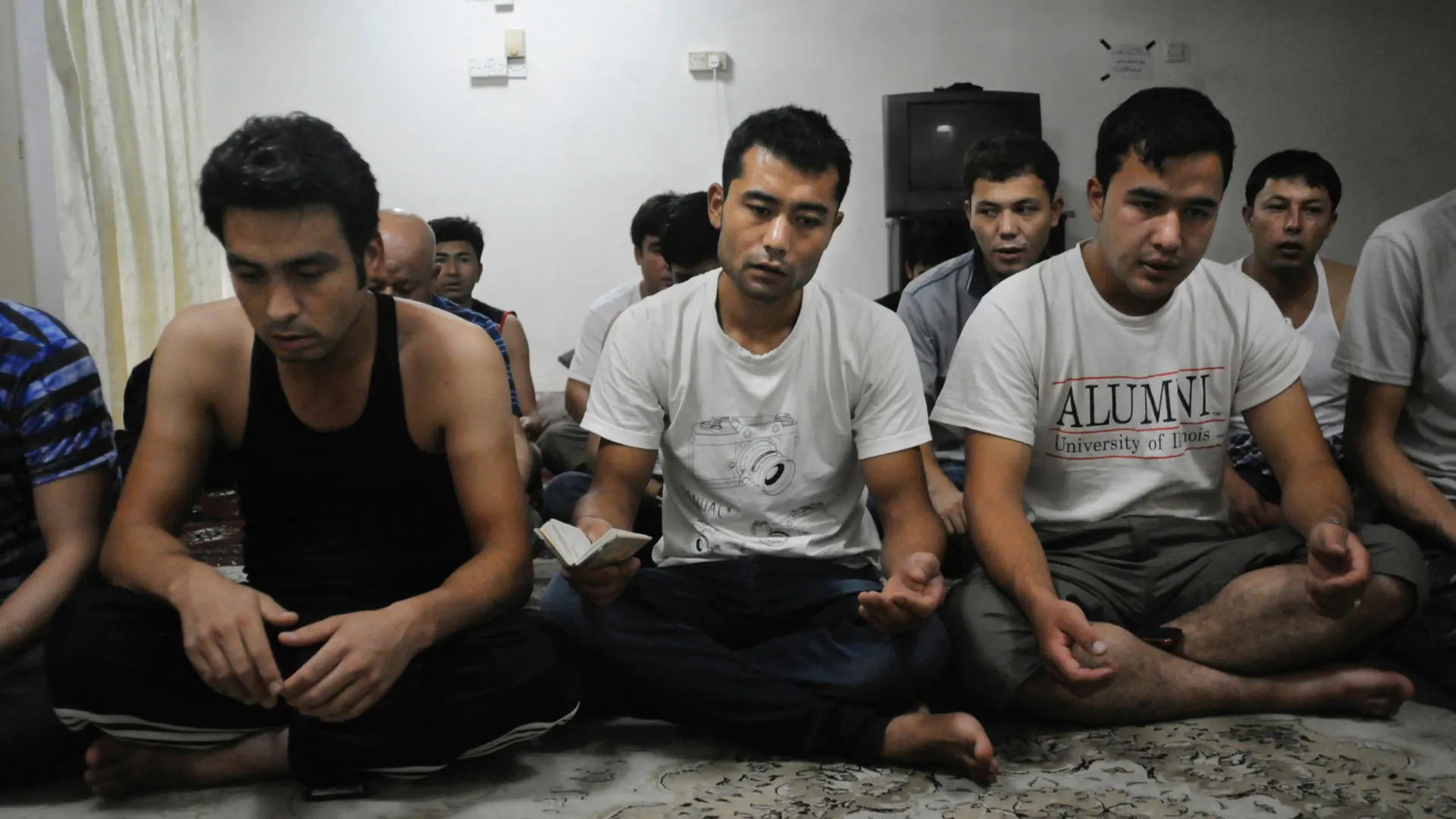 Asylum seekers sitting on the floor of a bare room in Kuala Lumpur, palms turned upward in prayer, 2012.