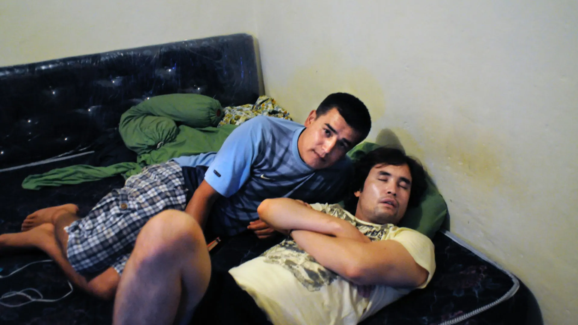 Two young men on a mattress in the villa at Bogor, one awake and one asleep, 2012.